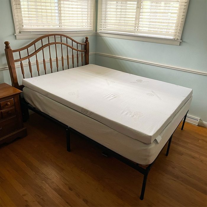 A bed with a wooden headboard stands in a corner room with light blue walls, accompanied by a wooden nightstand.