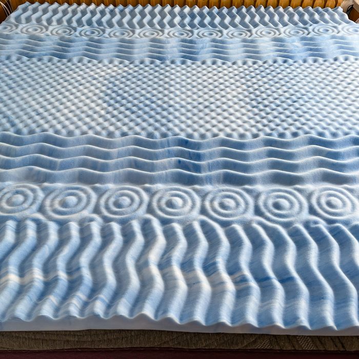 Foam mattress topper with textured wave patterns rests on a bed, featuring concentric circles and ridges.