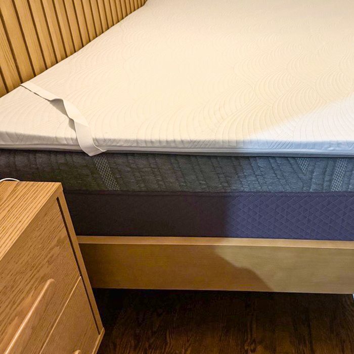 Bed with a thick mattress topper sits aligned next to a wooden nightstand in a cozy bedroom setting.