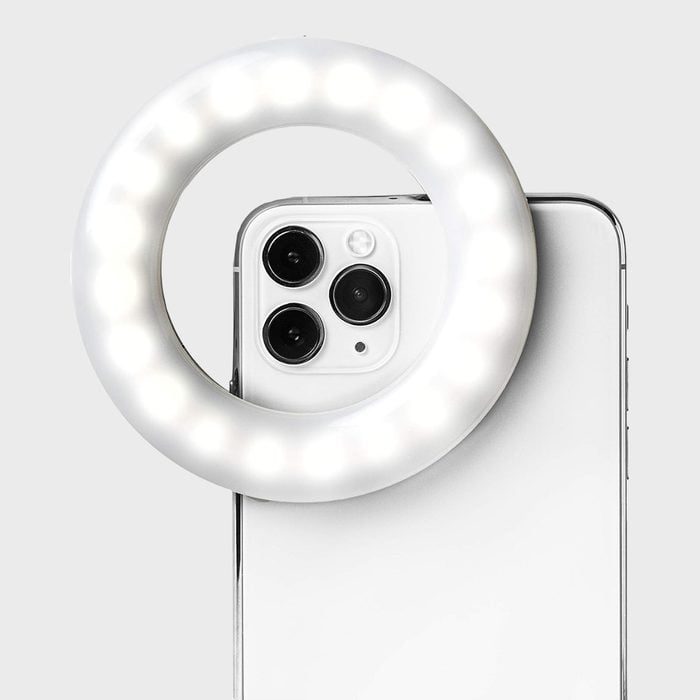 A smartphone with a glowing ring light attached over its camera lenses, shown against a plain gray background.