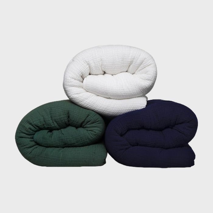 Three folded blankets in white, green, and navy are stacked together against a plain background.
