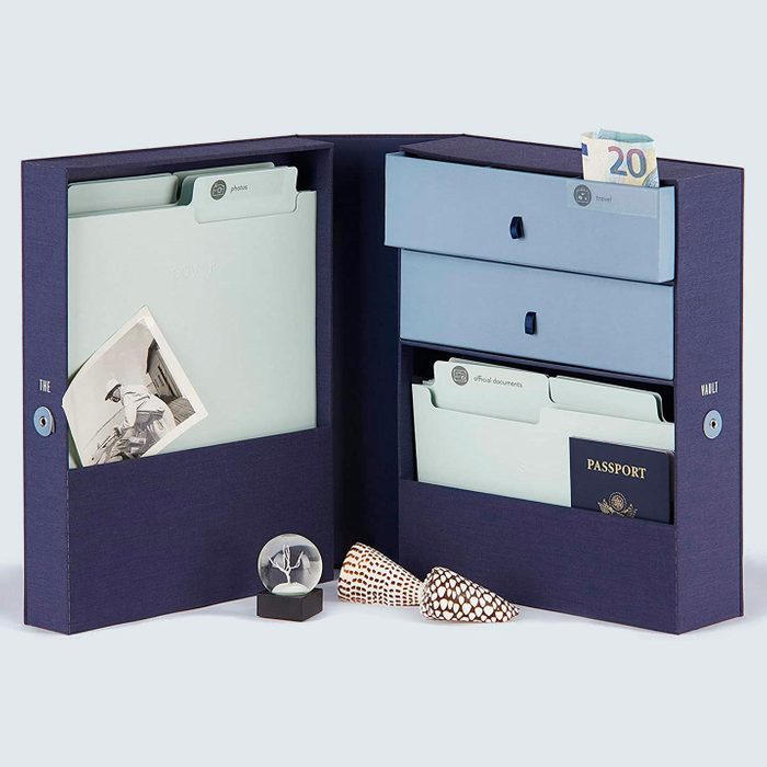 Open blue document organizer holding folders, a passport, and cash; features two shells and a small globe on a white surface.