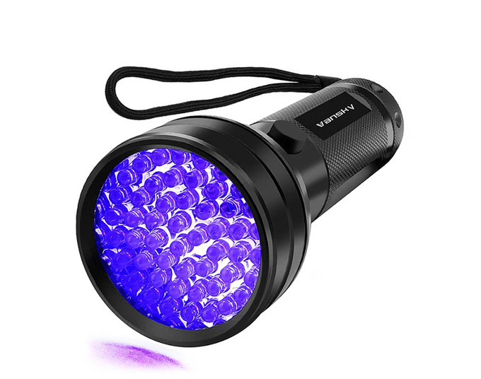 Flashlight emits purple light, resting on white background; features multiple LED bulbs, textured grip, and a black wrist strap. Text says 