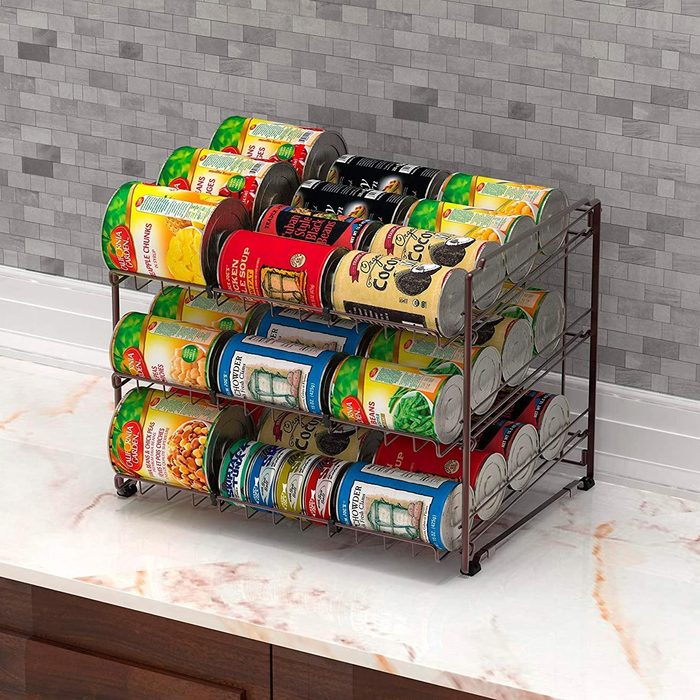 Cans are stacked neatly on a multi-tiered wire rack placed on a marble countertop against a tiled wall.