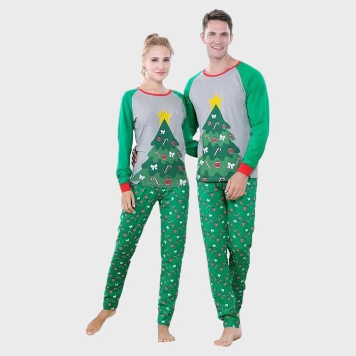 Two people wear matching Christmas tree pajamas, standing together on a plain white background.