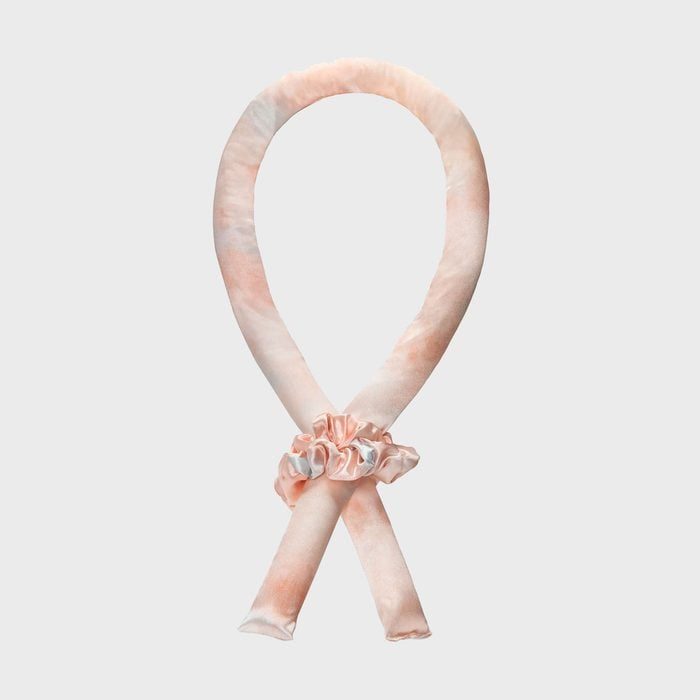 A soft, peach-colored hair roller looped in an infinity shape, held together with a matching scrunchie in a neutral-toned setting.