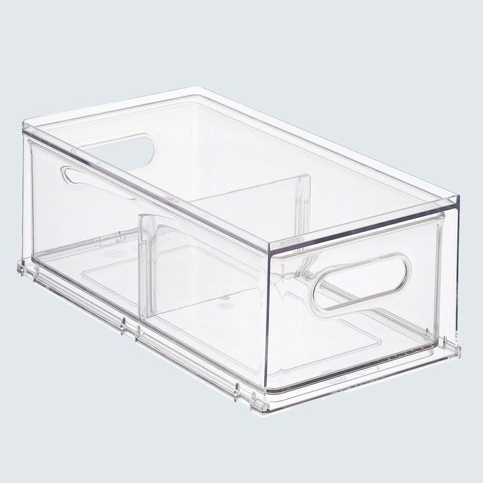 A clear plastic storage bin sits empty with side handles and internal dividers, placed against a plain, light gray background.