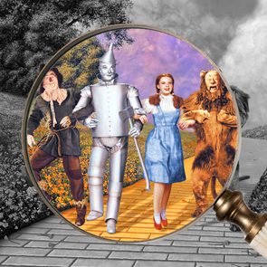 Magnifying glass reveals four characters walking on a colorful path, surrounded by grayscale scenery with trees and flowers.