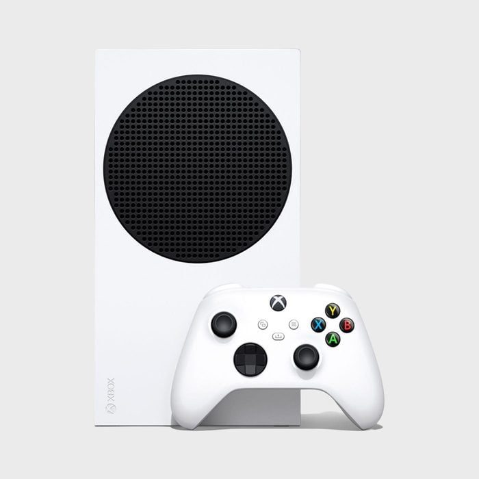 A white gaming console with a black circular vent stands upright, accompanied by a white controller on a plain background.