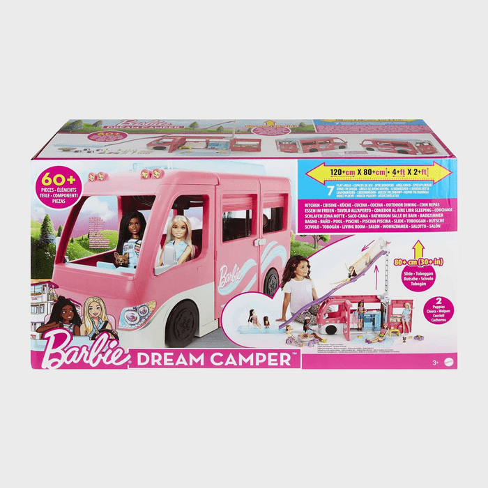 Pink toy camper on a box, showing Barbie dolls inside. Packaging describes features and includes colorful graphics and measurement details. 60+ pieces included.