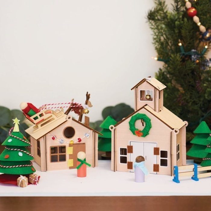 Wooden Christmas village display shows tiny houses, figures, and decorations; a festive scene with a tree and Santa's sleigh in a holiday setting.
