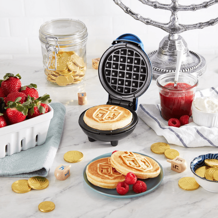 Waffle maker creates pancakes; set on a table with strawberries, jam, raspberries, and a jar of gold coins.