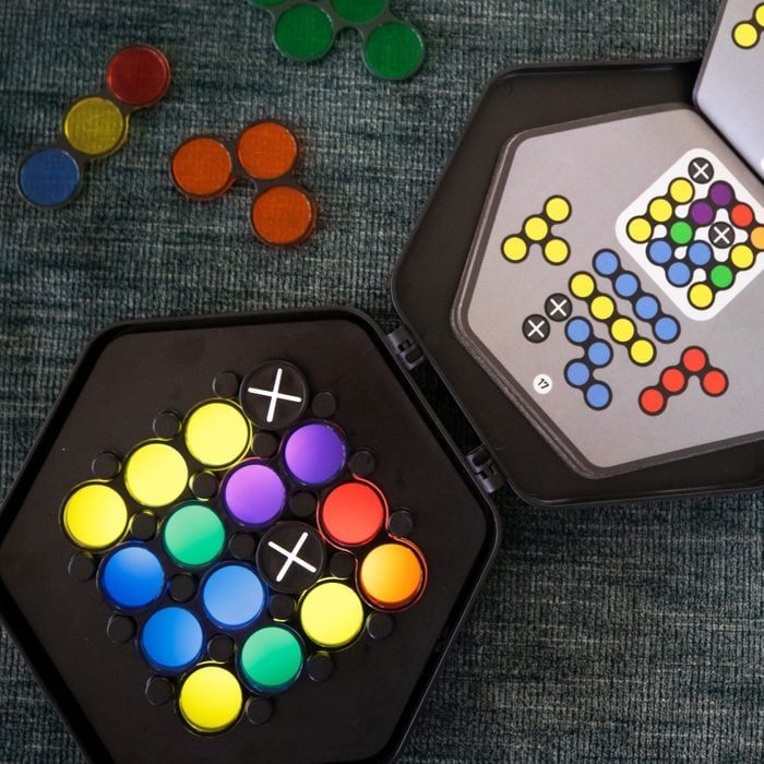 Colored circular tokens fill a hexagonal game board, with a card showing a color pattern. Tokens scattered on a textured surface.