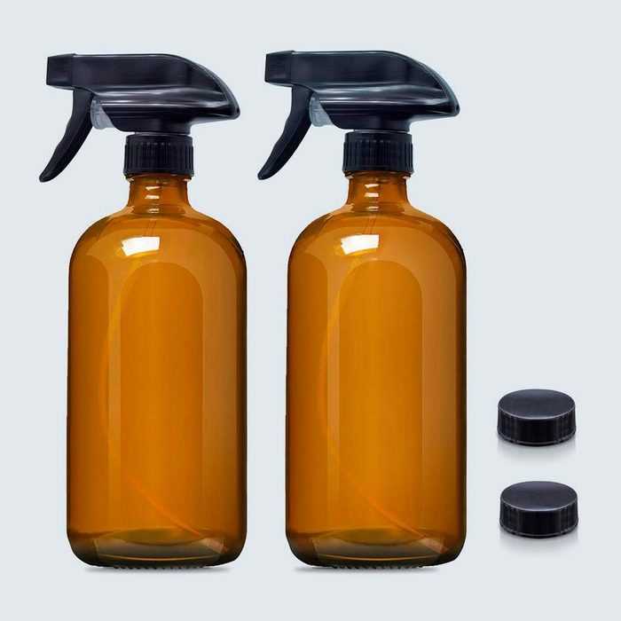 Two amber spray bottles with black trigger nozzles; two matching black caps lie nearby on a plain background.