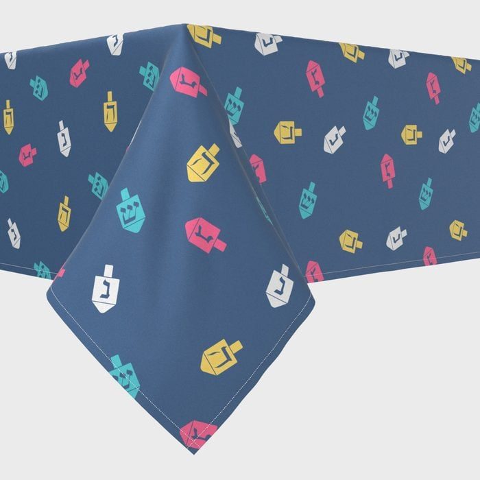 Blue tablecloth displaying colorful dreidel patterns with Hebrew letters in a simple, abstract design.