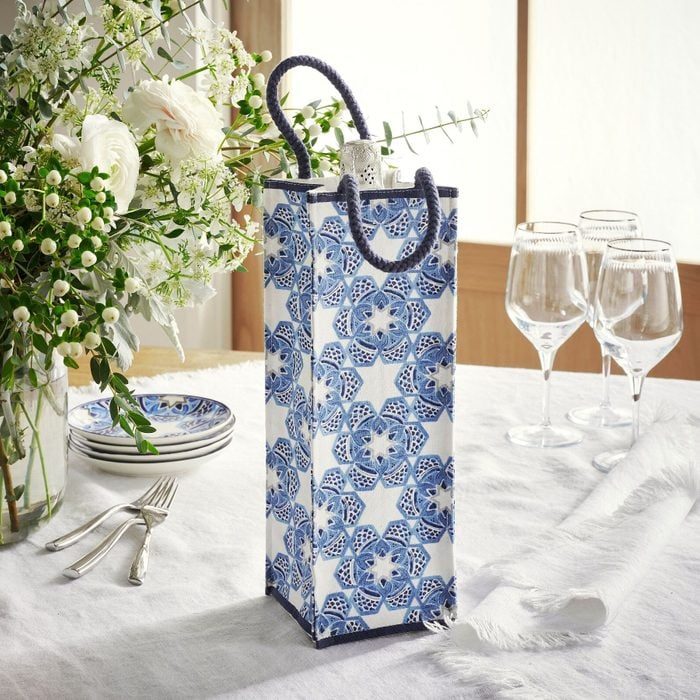 Decorative bag stands on table, featuring blue floral patterns, amidst white flowers in a vase, glassware, and stacked plates with cutlery nearby.