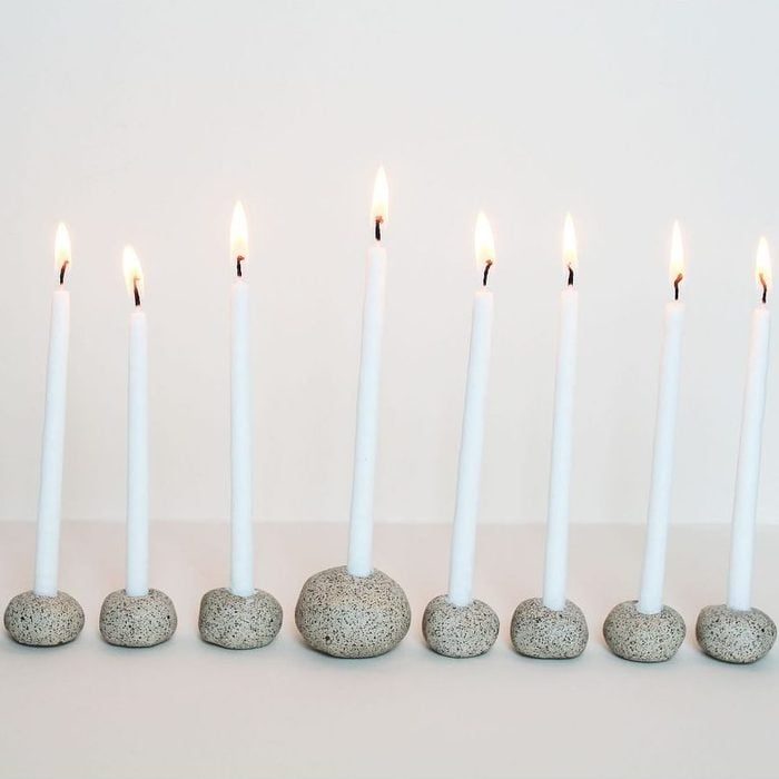 Candles are lit, arranged in a row on textured stone holders, set against a plain background.