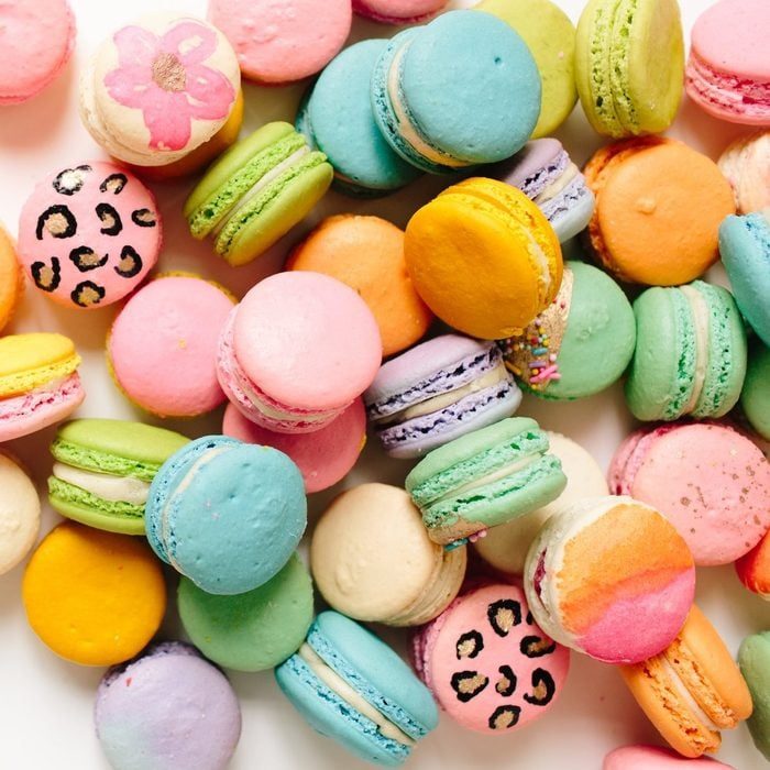Colorful macarons are scattered, showcasing various pastel hues and patterns, set against a plain, light background.