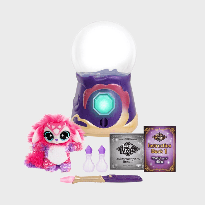 A crystal ball rests on a colorful base, surrounded by a pink plush creature and magic-themed instruction books and accessories.