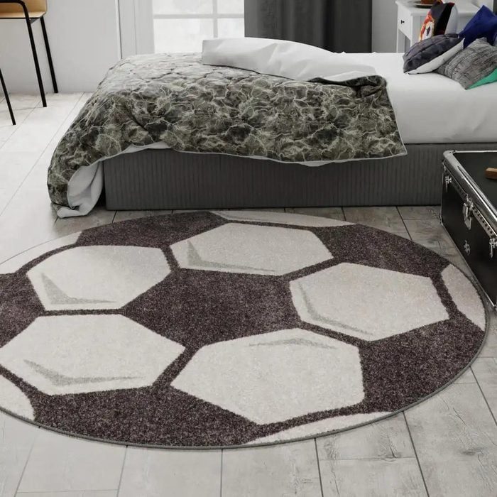 Rug lies on floor, resembling a soccer ball pattern, beside a bed with a textured blanket in a bedroom setting.