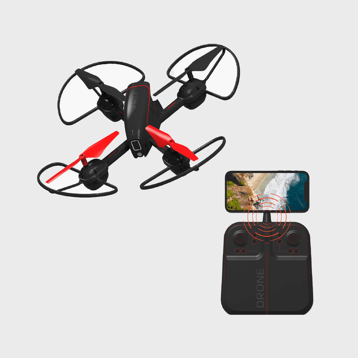 Drone hovering, with red and black propellers, near a remote control displaying a beach view on a connected smartphone screen.