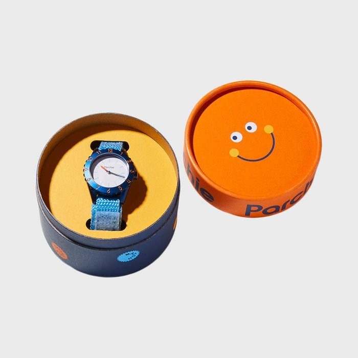 Watch with a blue strap sits in circular box; lid shows smiley face design and text 