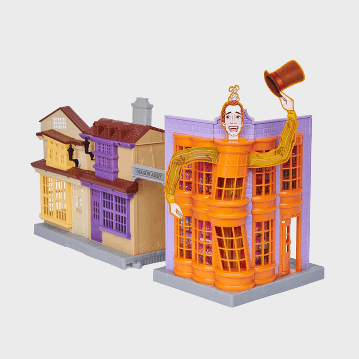 Model buildings stand on a grey base; one features an orange storefront with a character holding a top hat. Sign reads 