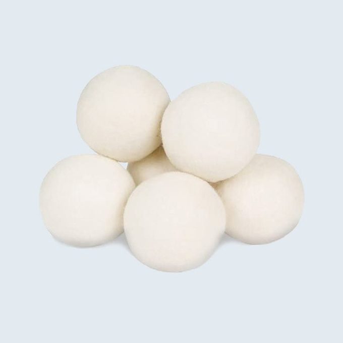 Six white wool balls are stacked, resting against a soft, light blue background.