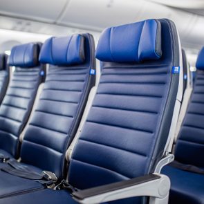 Airplane seats, unoccupied, arranged in a row within a well-lit cabin, featuring blue upholstery and seatbelts.