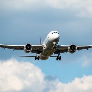 Airplane flying, approaching for landing, in a partly cloudy sky background.