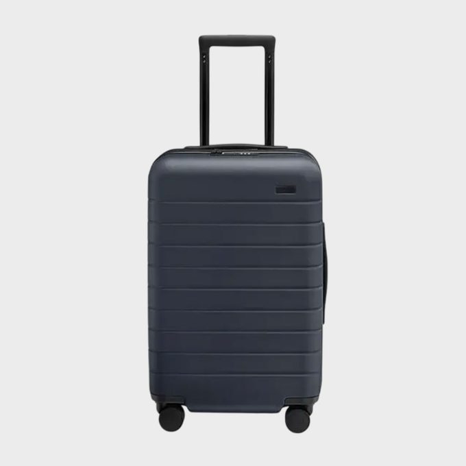 A navy blue suitcase stands upright, featuring an extended handle and four wheels, against a plain white background.