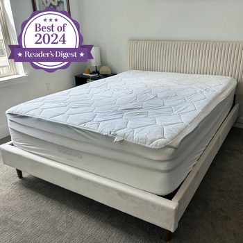 Mattress sits on a modern bed frame in a bright bedroom. "Best of 2024 Reader's Digest" emblem displayed in the top left corner.