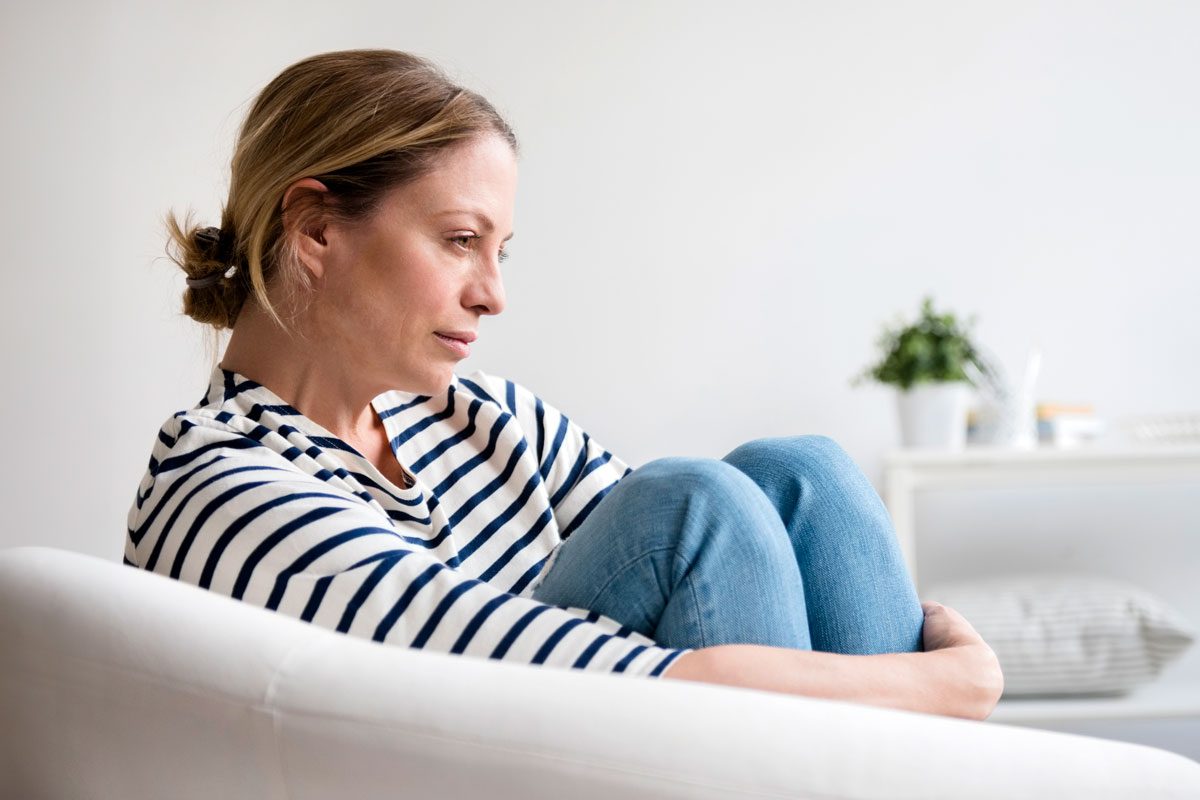 Depressed Woman Sitting In Armchair Holding Legs