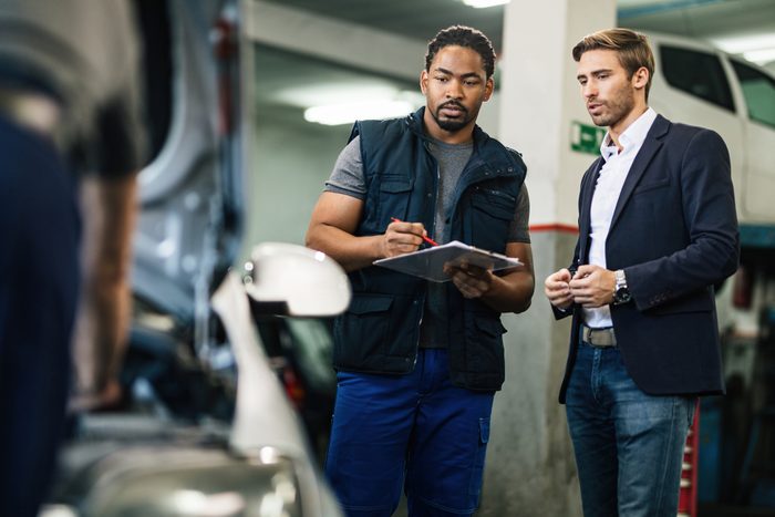 Young businessman communicating with his car repairman about vehicle breakdown at workshop.