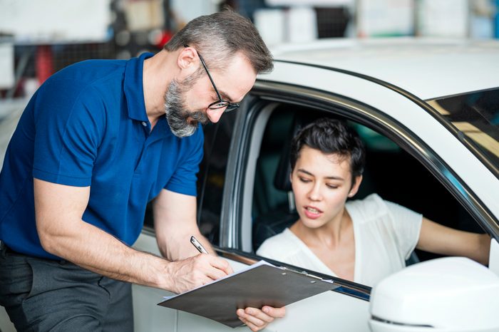 Caucasian auto mechanic with female client looking at car checklist with bill at Auto Repair Center. Female client sitting in car. Customer Service, Quality of Service.