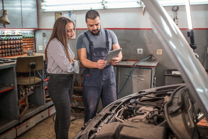 Car mechanic with tablet showing the problems to woman customer in auto repair shop