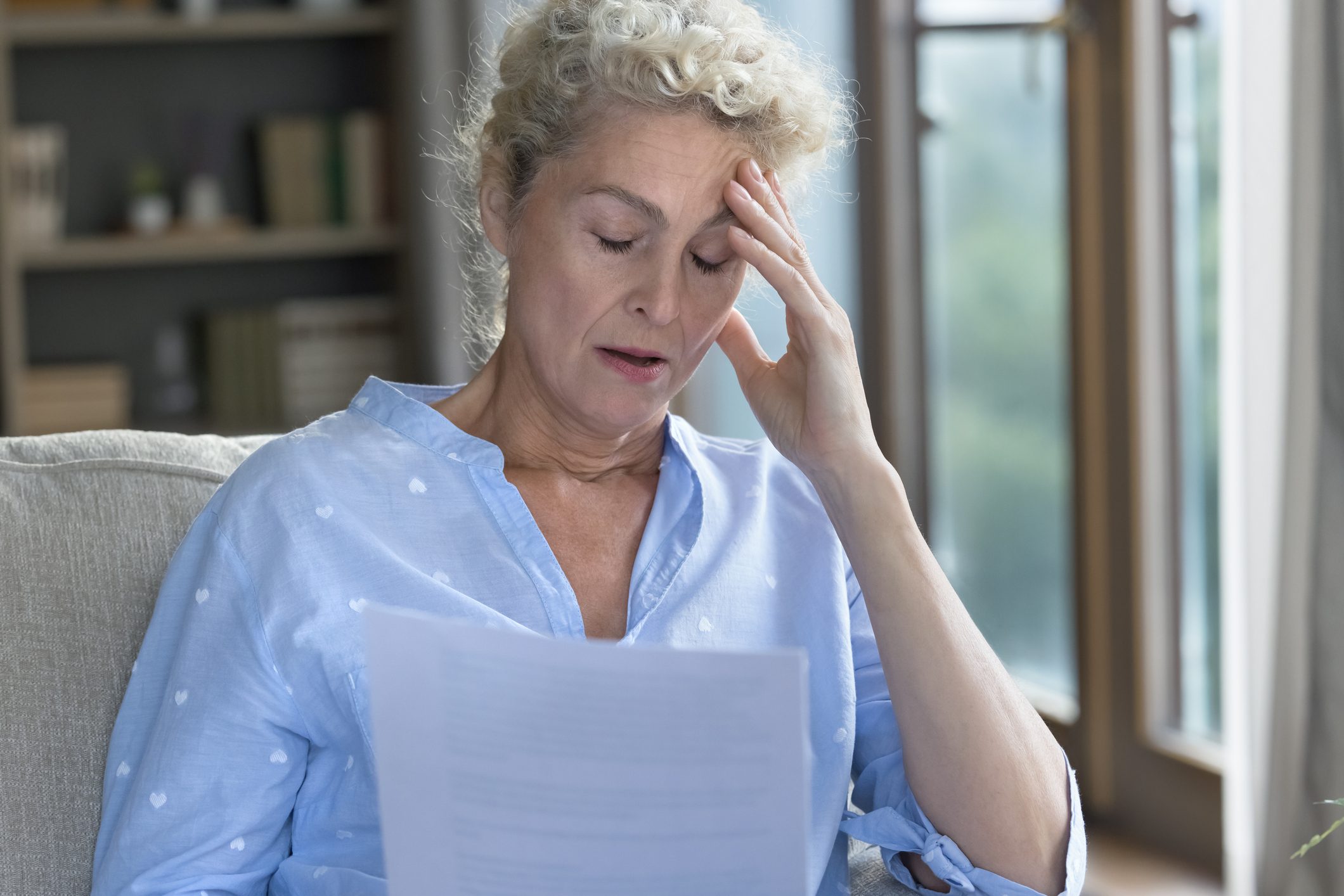 Shocked older woman holding paper legal document on home sofa