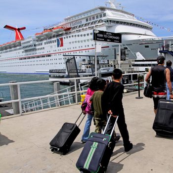 Passengers with suitcases walk along dock toward Carnival cruise ship