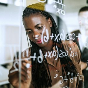 Woman writing Mathematical Formulas On Transparent Wipe Board