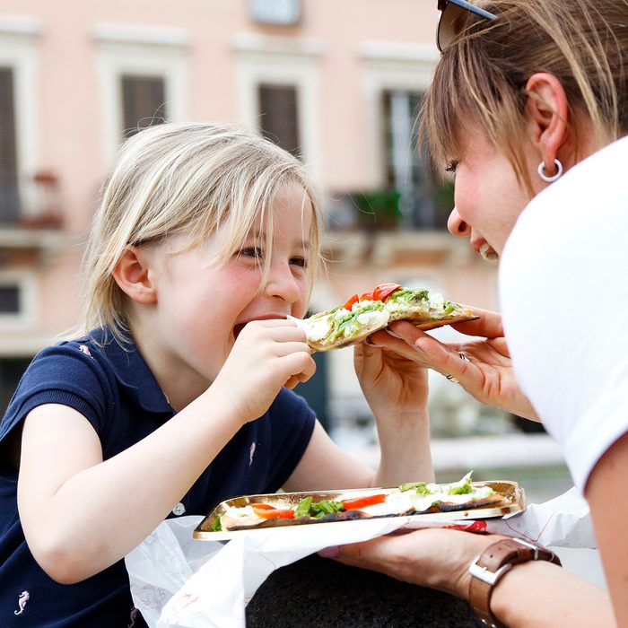 Young girl eating pizza and smile to his mother
