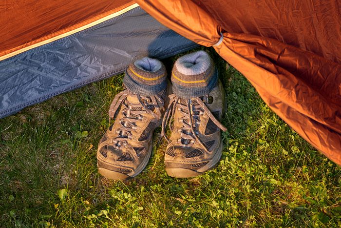 Hiking boots with patterned socks stuffed inside resting on grass outside an orange tent.