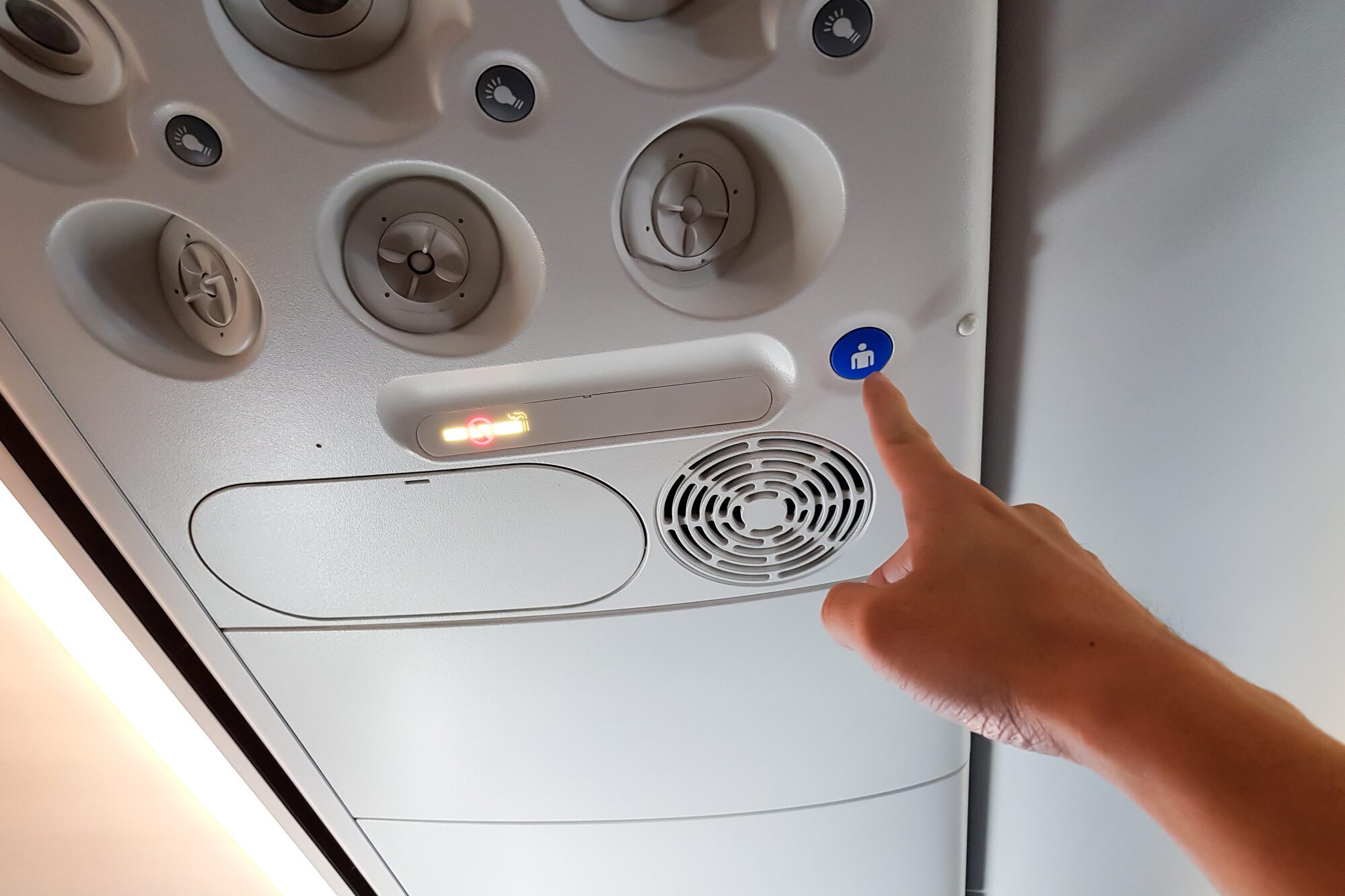 Hand pressing the blue flight attendant call button on an airplane ceiling