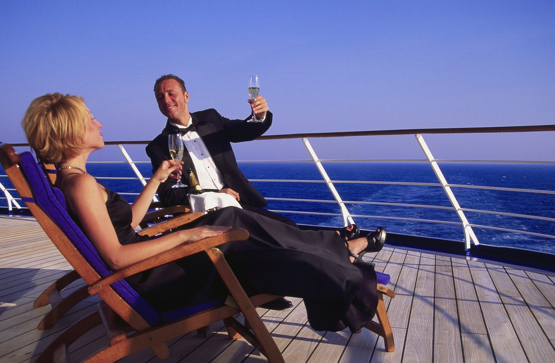 couple dressed in formal wear toasting champagne in lounge chairs on the deck of a cruise ship