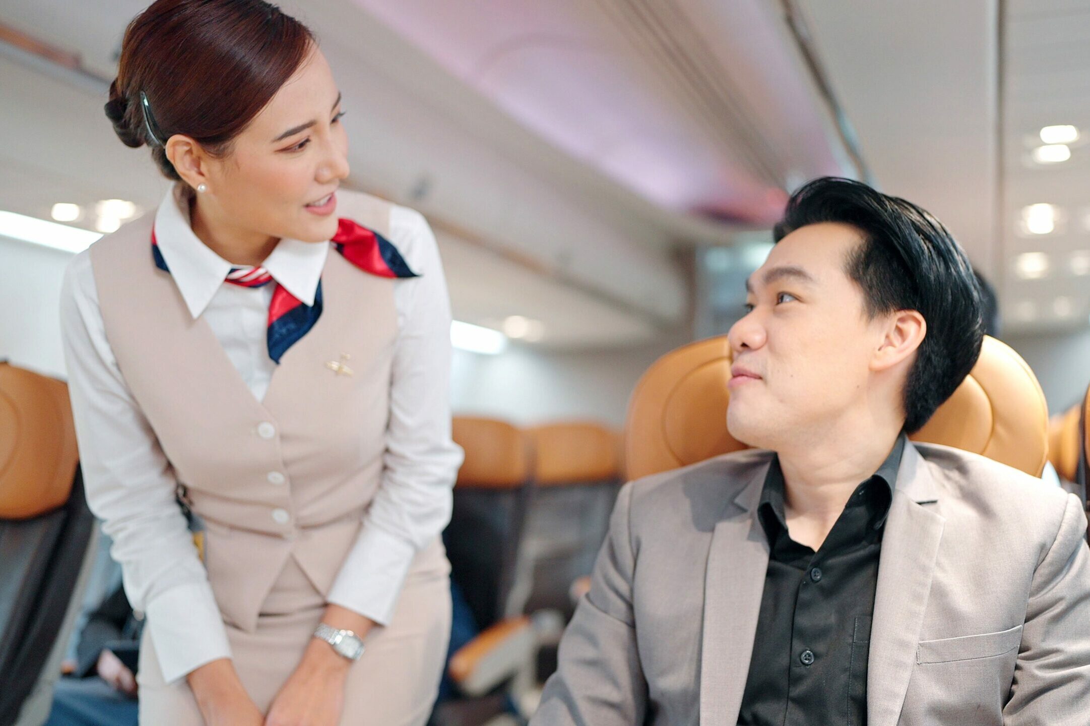 Flight captain or stewardess in air hostess uniform talking with passengers on airplane