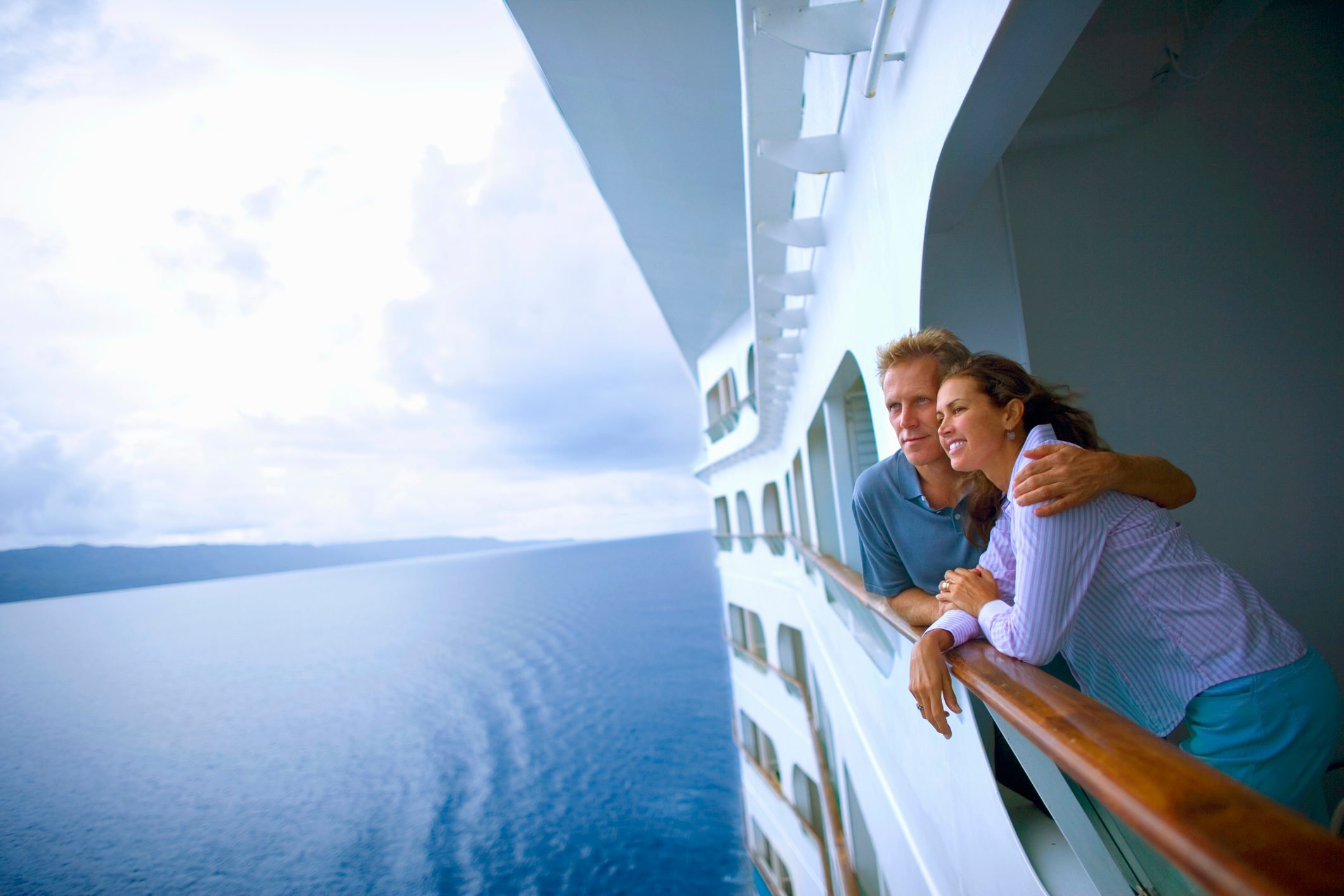 Couple leaning on rail of cruise ship, looking at ocean