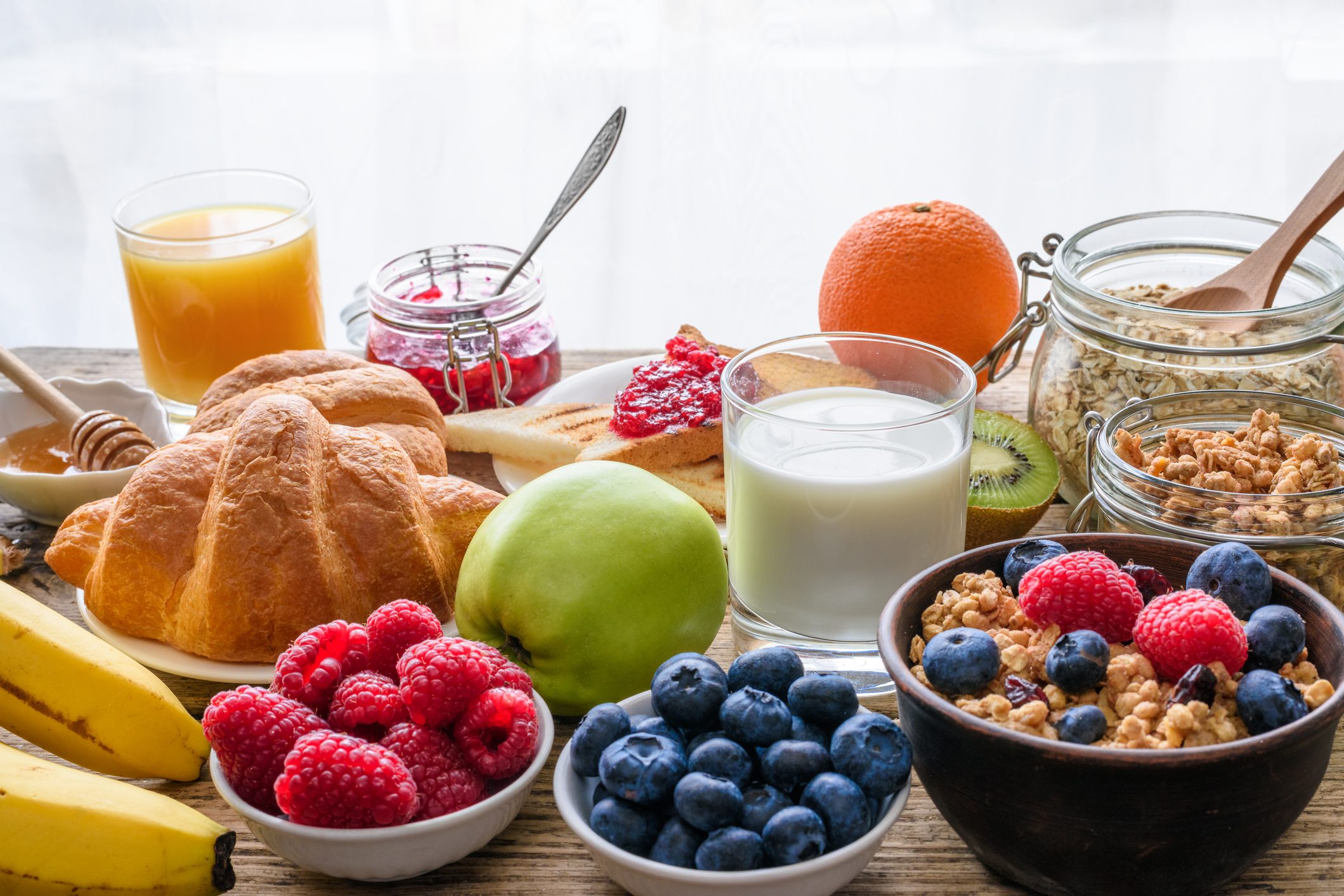 Healthy breakfast buffet with various morning food and drinks. Oats, granola, croissant, milk, oatmeal, toast, fruit, berries, nuts, orange juice. Assortment of tasty vegetarian food