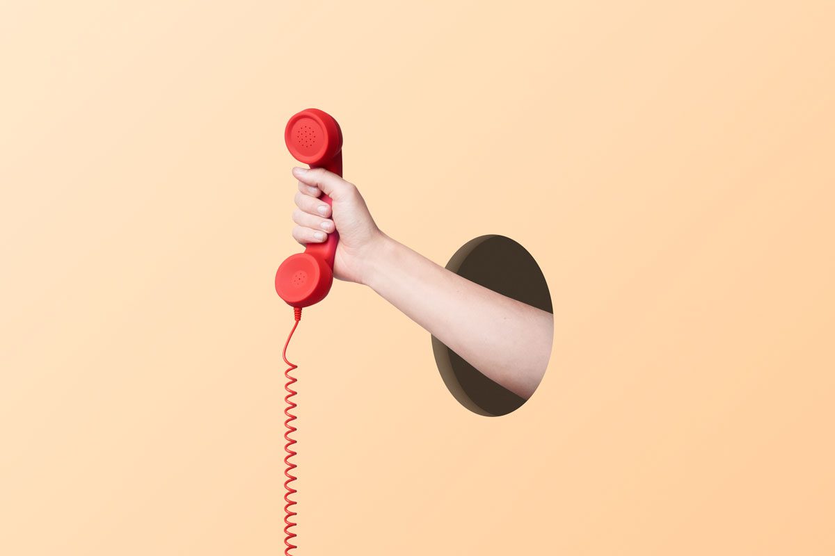 Hand Coming Out From Hole In The Wall And Holding A Red Phone
