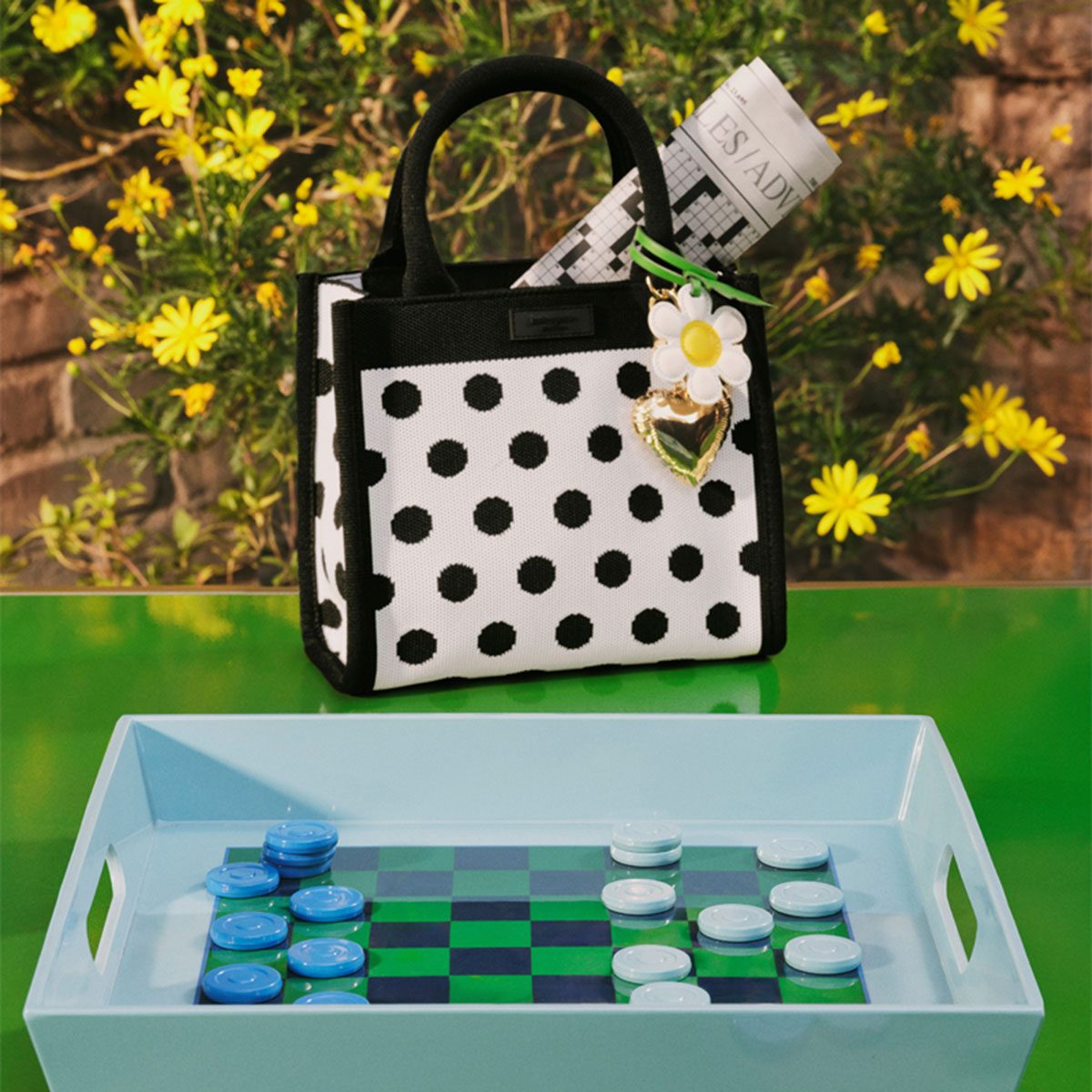 Kate Spade purse with a checker board on a green table with yellow flowers in background