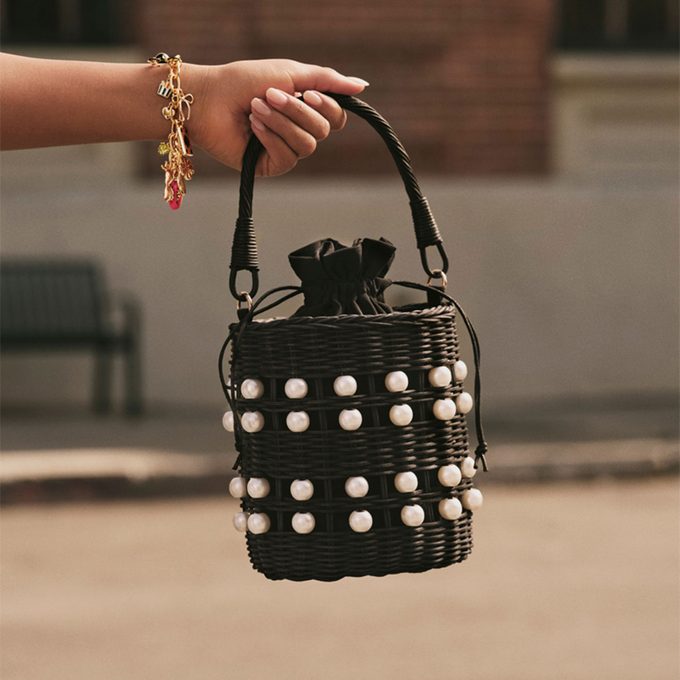 Hand holding a black wicker purse with white polka dots